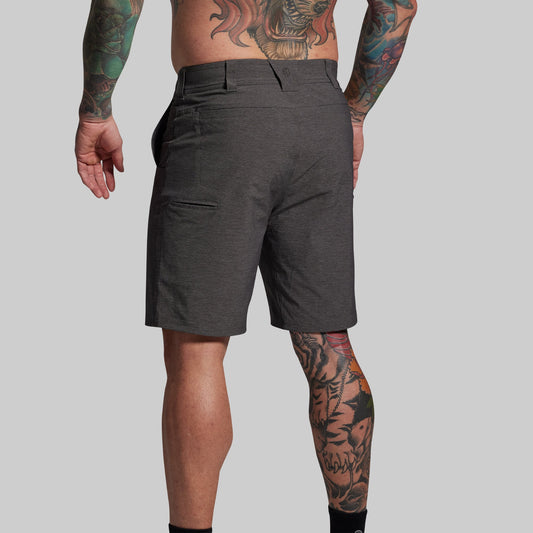 Person wearing dark gray shorts with tattoos on arms and legs against a plain background