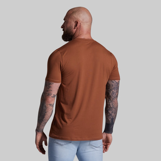 Man wearing a brown t-shirt and light blue jeans against a plain background