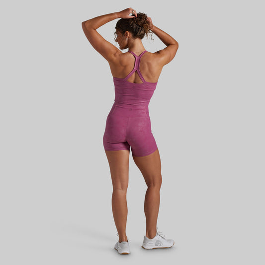 A woman viewed from the back wearing a fitted athletic set in a dusty mauve-purple color, paired with white sneakers.