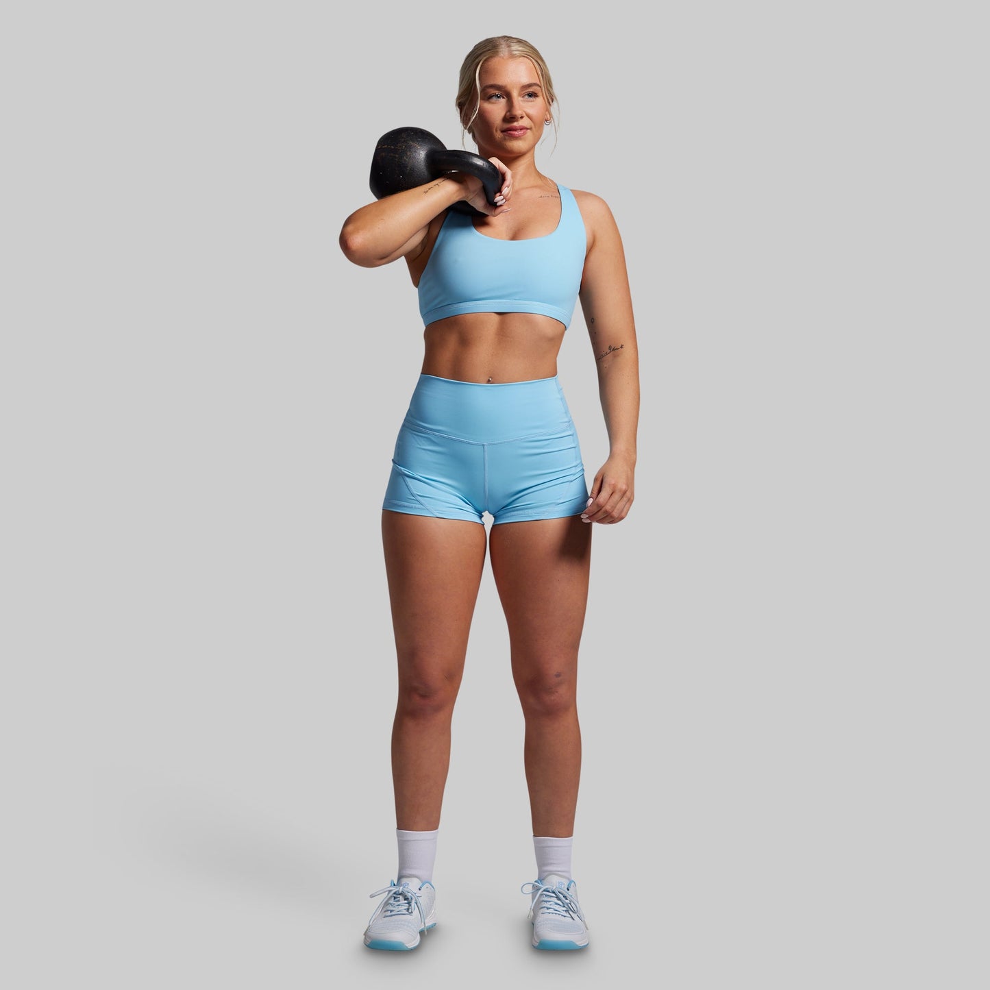 Woman in blue athletic wear holding a kettlebell against a gray background