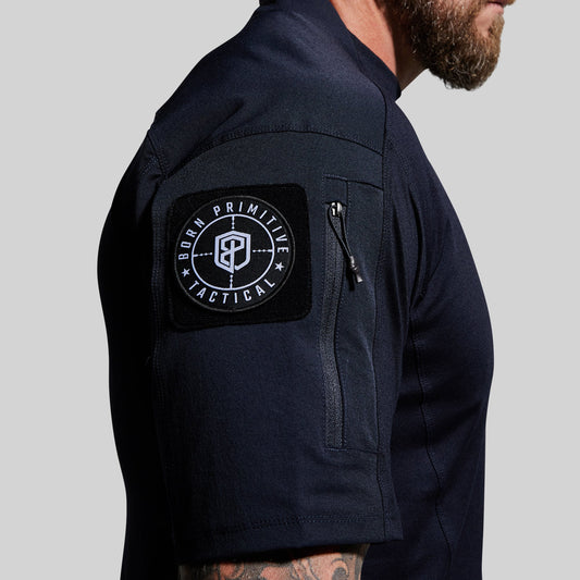 Person wearing a blue tactical shirt with a visible brand patch on the sleeve against a gray background