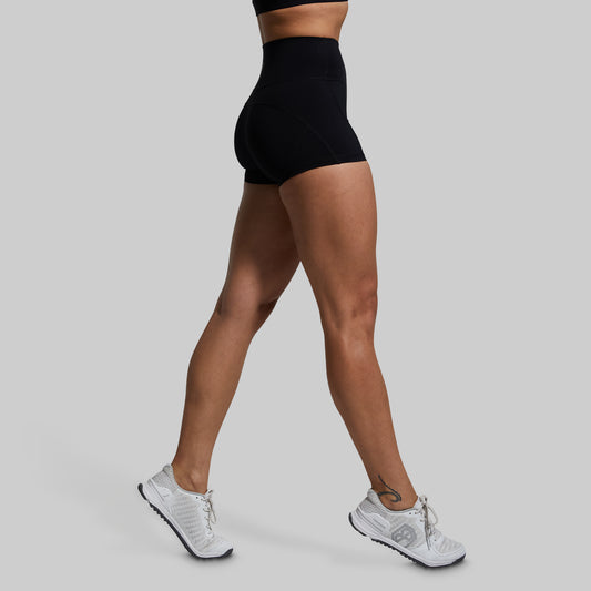 Person wearing black high-waisted shorts and white sneakers on a gray background