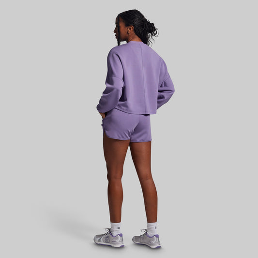 Person wearing a purple sweatshirt and shorts set on a light gray background