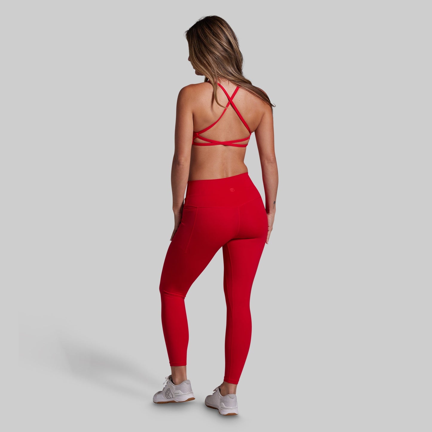 Woman wearing a red sports bra and leggings set on a gray background