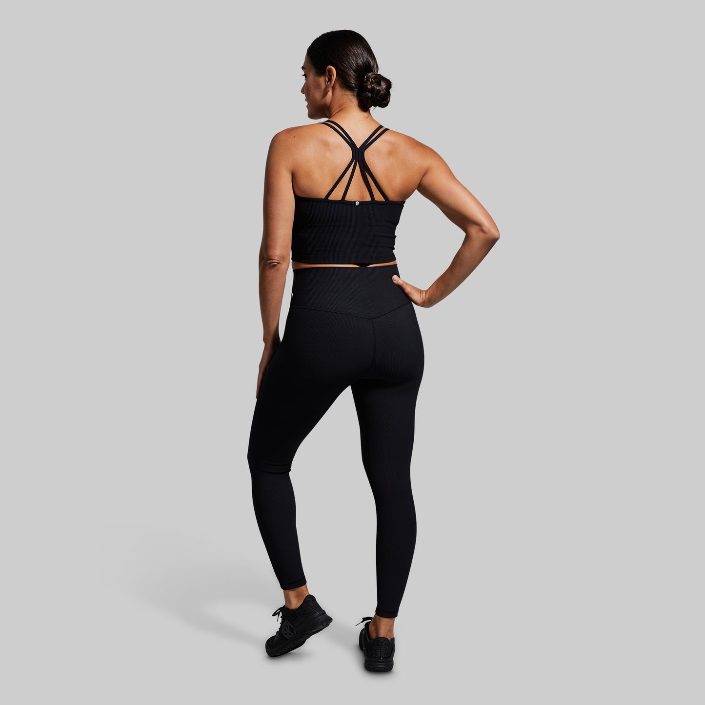 Woman wearing a black sports bra and leggings set on a gray background