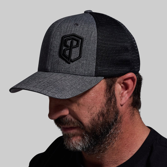 A person wearing a two-tone trucker hat with mesh side panels in charcoal and black colors.