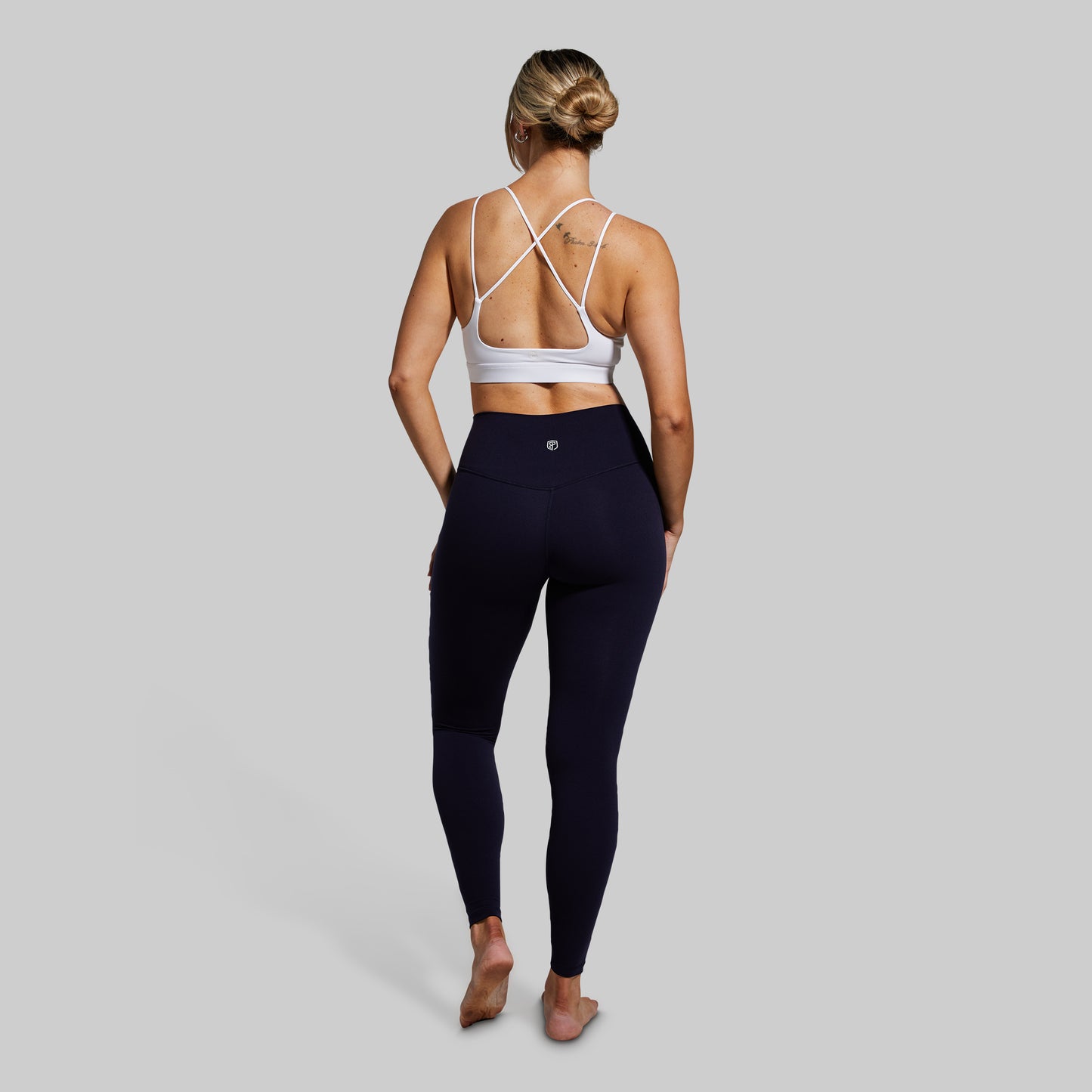 Person wearing a white sports bra and navy leggings on a gray background