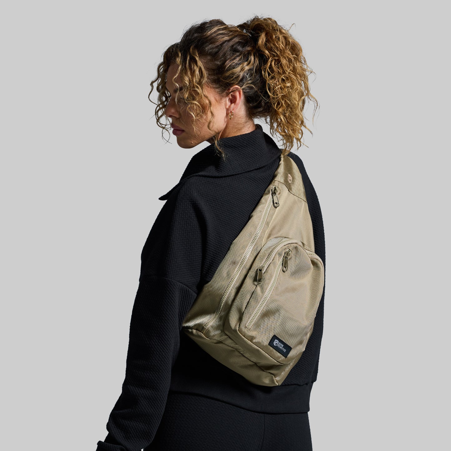Person wearing a beige sling bag on a plain background