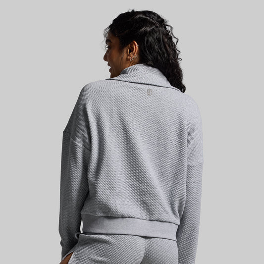 Person wearing a gray textured sweater against a plain background