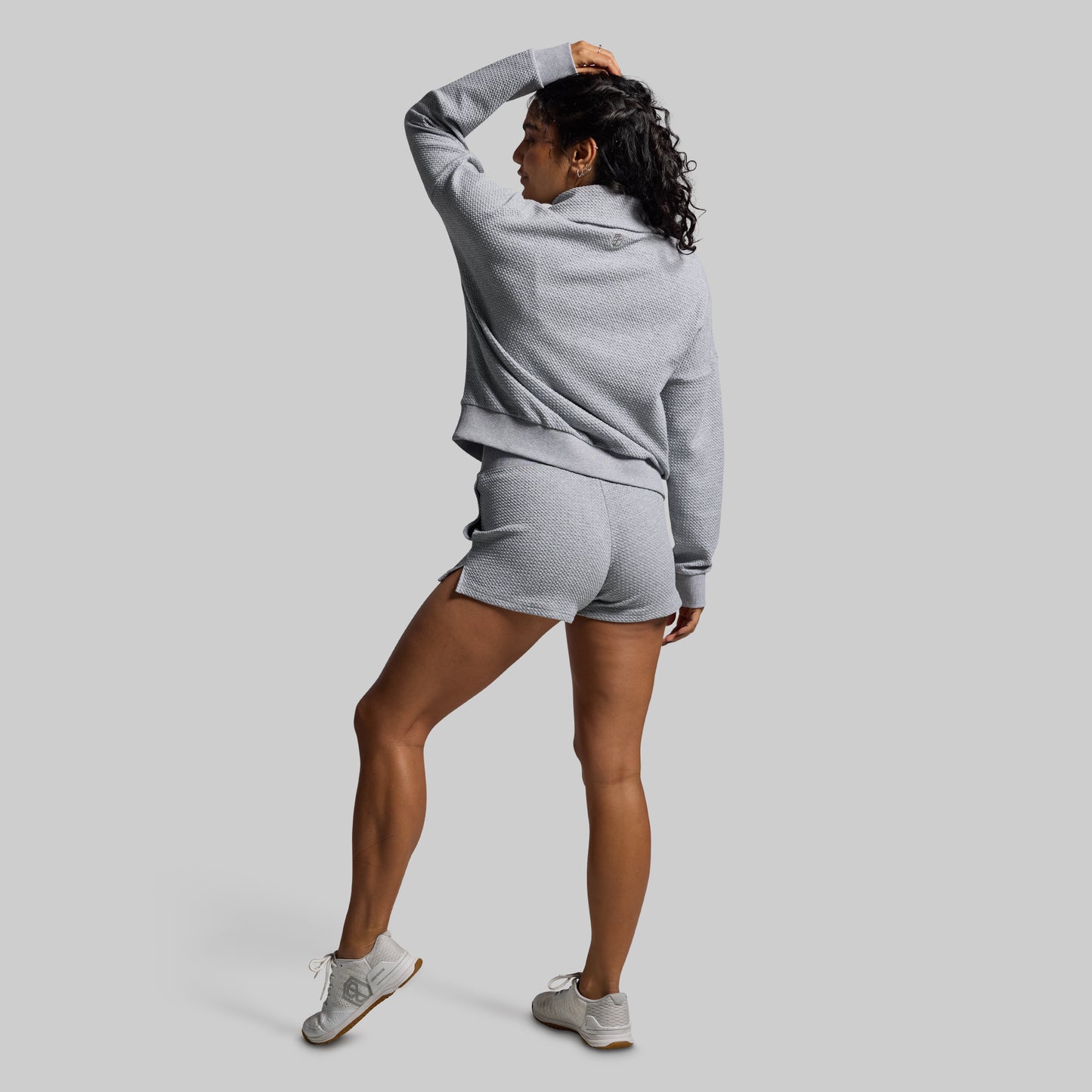 Woman wearing a gray sweatshirt and shorts set on a light gray background