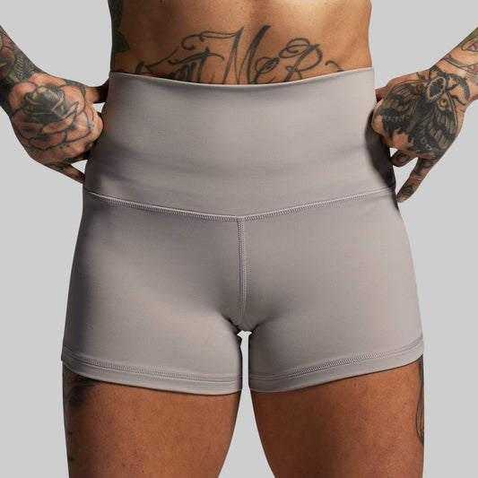 Person wearing gray shorts with tattooed arms on a plain background