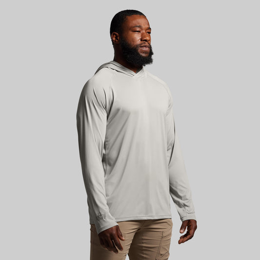 Man wearing a light gray hoodie and beige pants against a plain background
