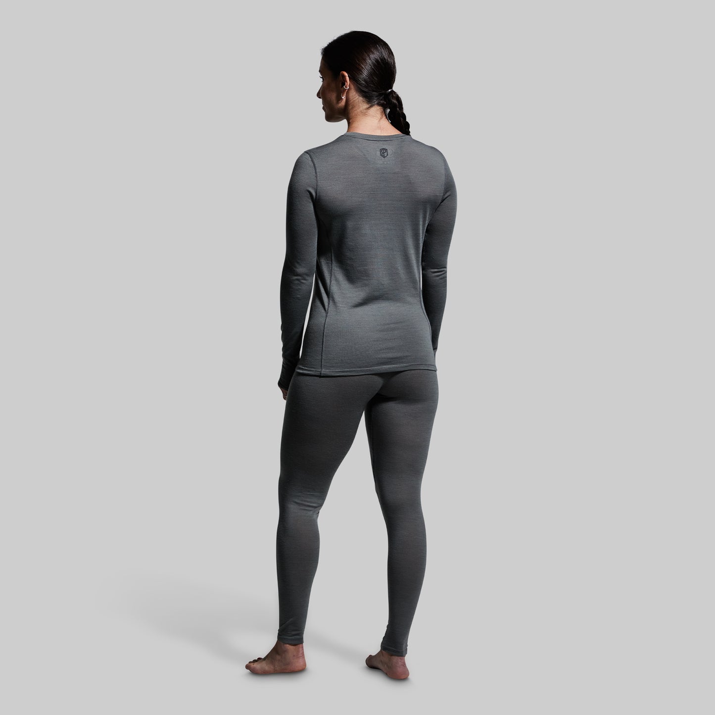Woman wearing gray base layer bottoms and long sleeve top on a plain background