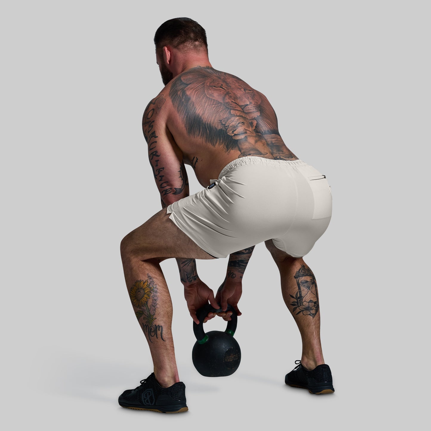 Man lifting a kettlebell wearing a white shorts with a unique design on a gray background