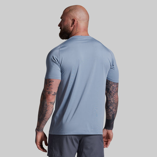 Man wearing a light blue athletic shirt and dark gray shorts on a plain background