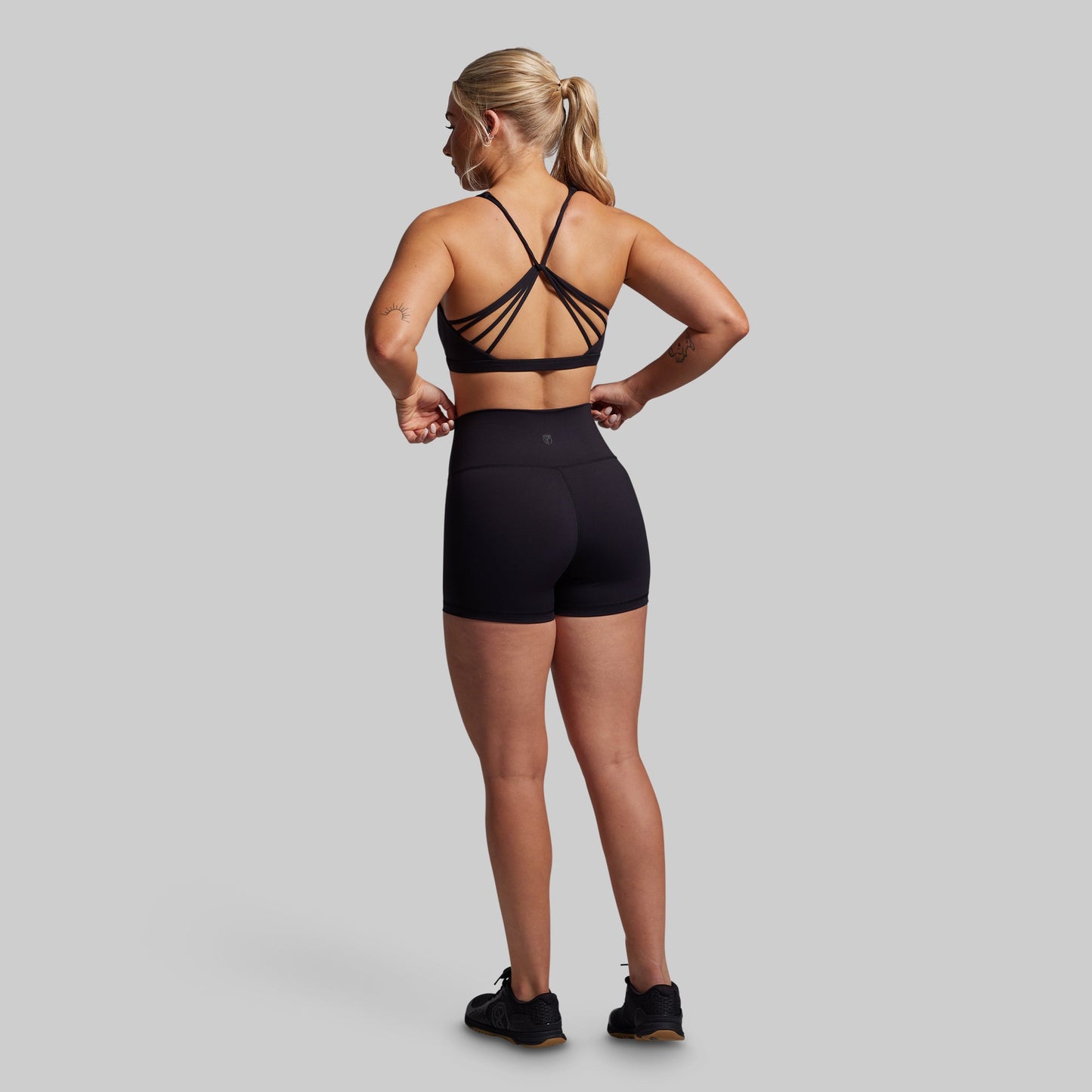 Woman wearing a black sports bra and shorts on a gray background