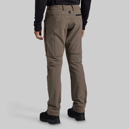 Rear view of a person wearing grey technical cargo pants with black boots and a black long-sleeve top, shown against a light gray studio background.
