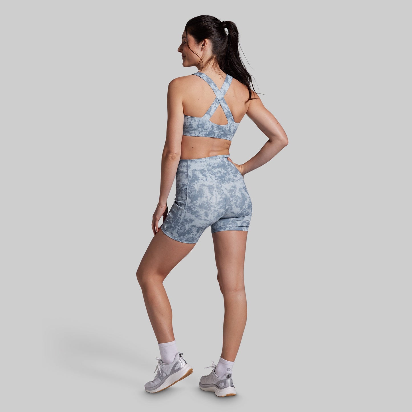 Woman wearing a gray tie-dye sports bra and shorts set on a light gray background