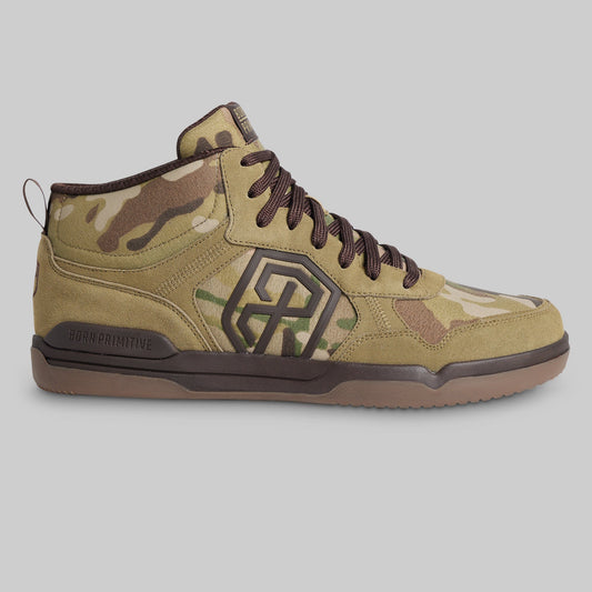 A mid-top sneaker from the brand BORN PRIMITIVE, featuring a tan and brown camouflage pattern with dark brown laces, a dark brown geometric logo on the side, and a brown outsole, shown against a solid gray background.