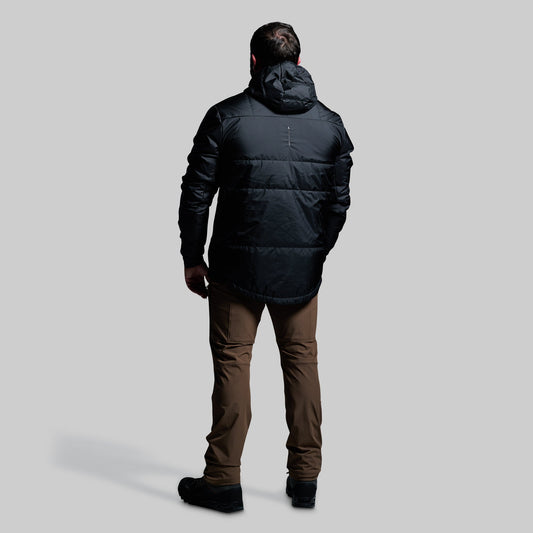 Person wearing a black puffer jacket and brown pants on a light gray background