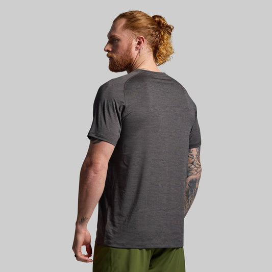Man wearing a dark gray t-shirt and green pants against a plain background