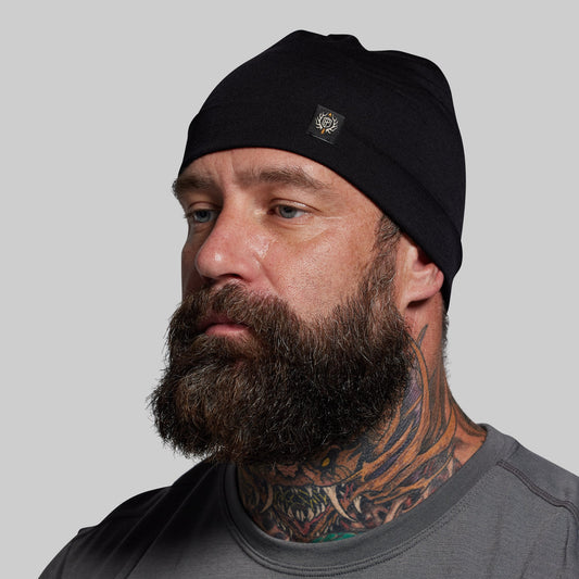 Man wearing a black beanie with a logo on a gray background