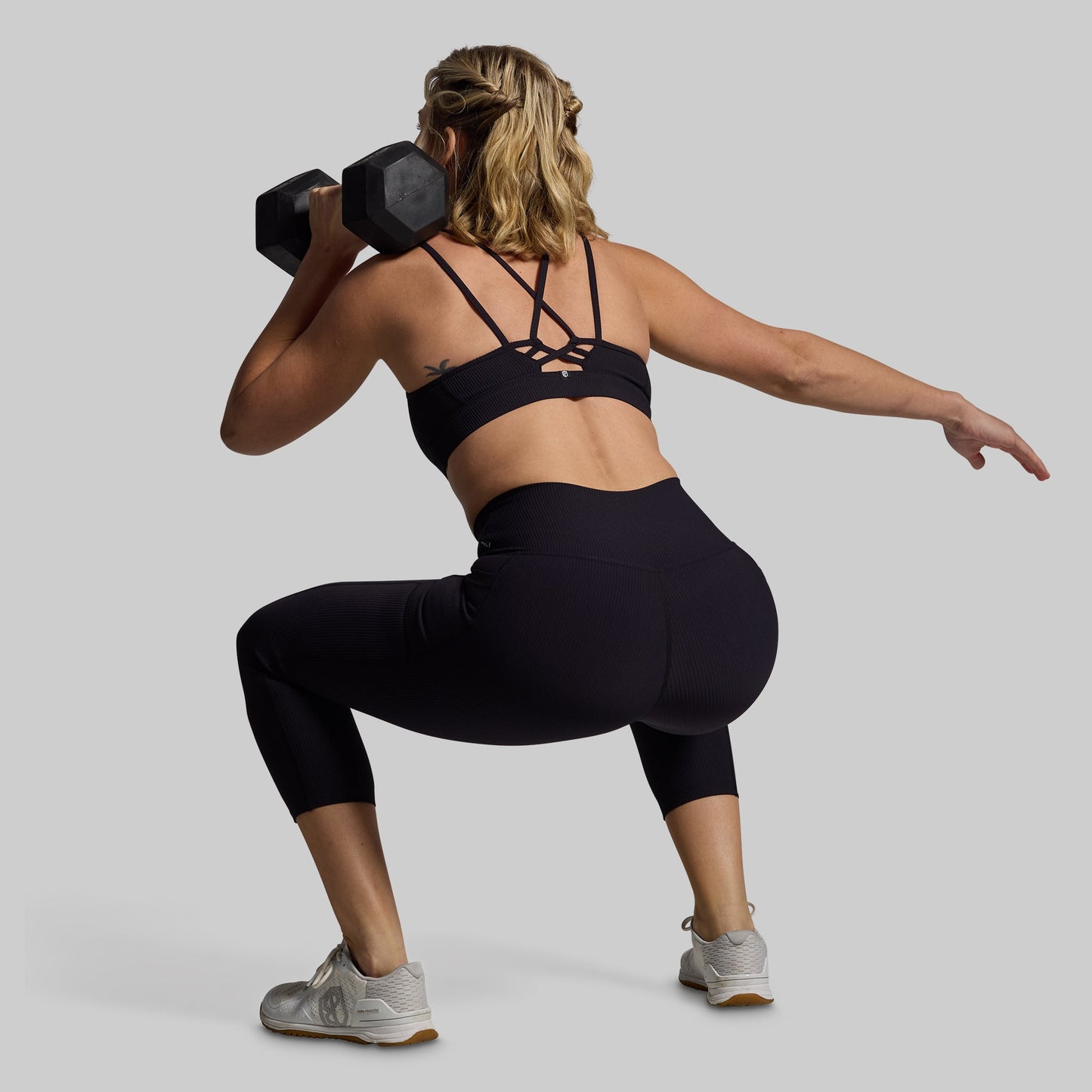 Woman squatting with dumbbell in black sports bra and capris.
