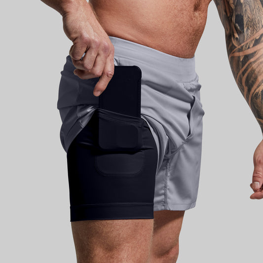 Person wearing gray shorts with a black compression liner pocket on a plain background
