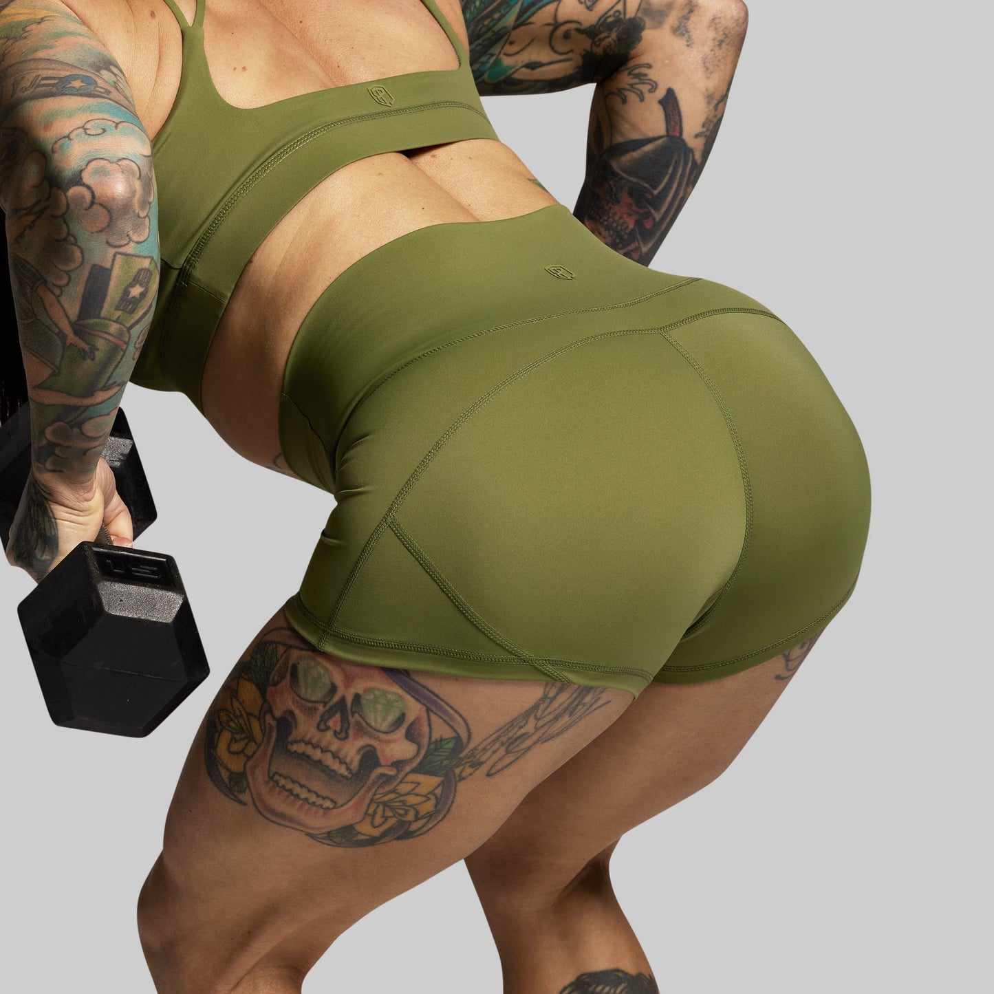 Person wearing green athletic wear holding a dumbbell on a gray background