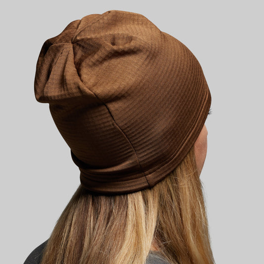 Brown ribbed knit beanie worn by a person with blonde hair on a gray background