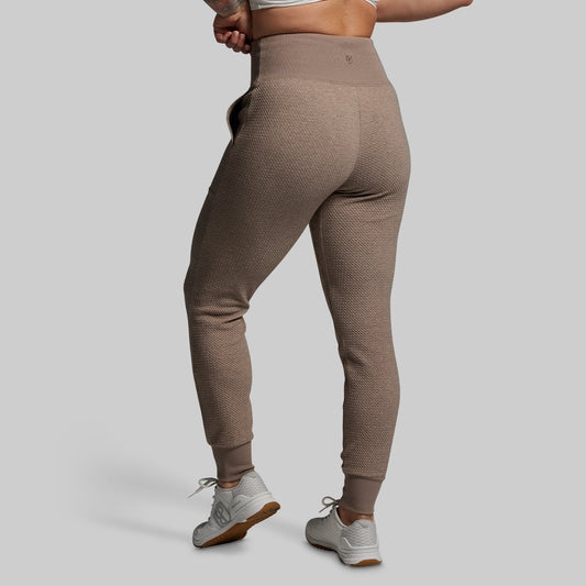 Person wearing brown textured joggers on a plain background