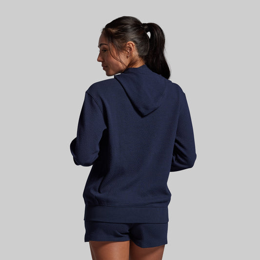 Person wearing a navy blue hoodie and shorts set on a gray background