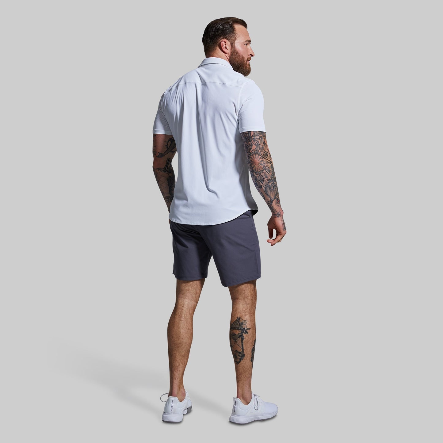 Man wearing a white shirt and dark shorts against a plain background