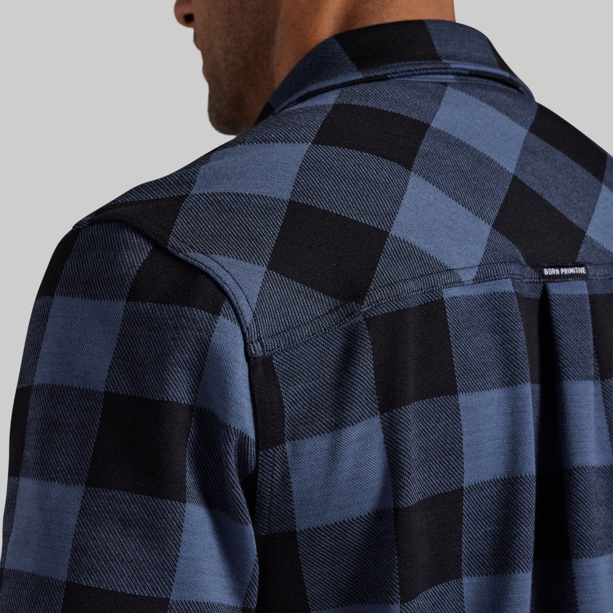 Close-up of a man wearing a blue and black buffalo plaid flannel shirt, showing the back of the neck, collar, and shoulder.
