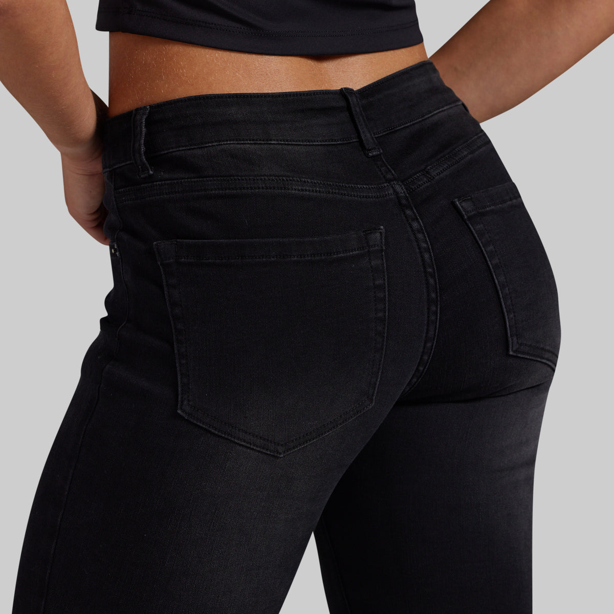 Close-up back view of a person wearing black high-waisted skinny jeans, showing the back pockets and waistband against a light gray studio background.