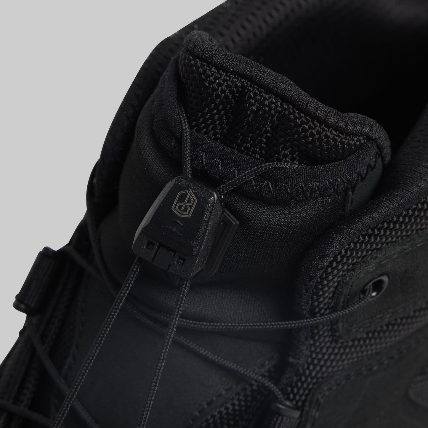 Close-up of a black tactical boot with a brand logo on a gray background