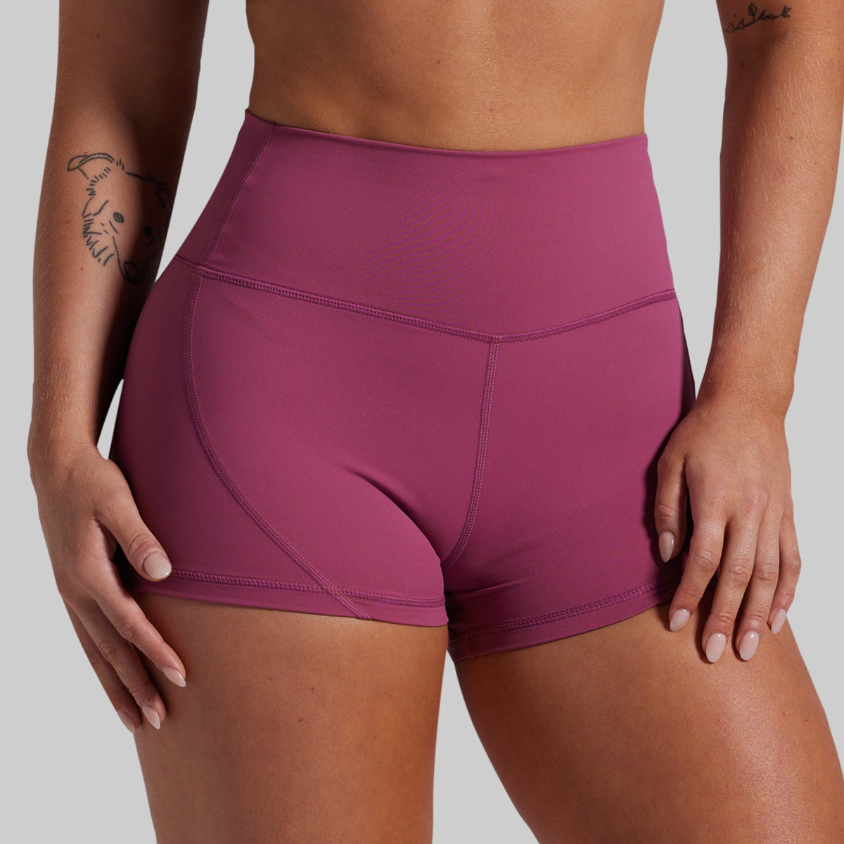 A close-up of a model wearing high-waisted athletic shorts in a dusty rose or mauve color, shown from the waist to the upper thighs against a solid light gray background.