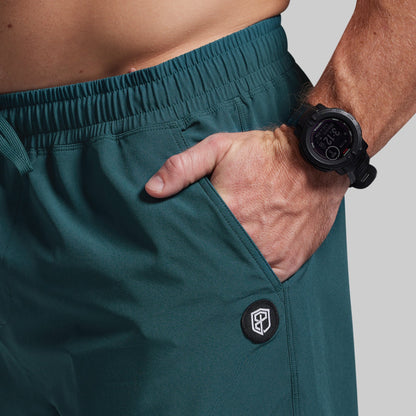 Person wearing teal shorts with a brand logo, holding a black watch.