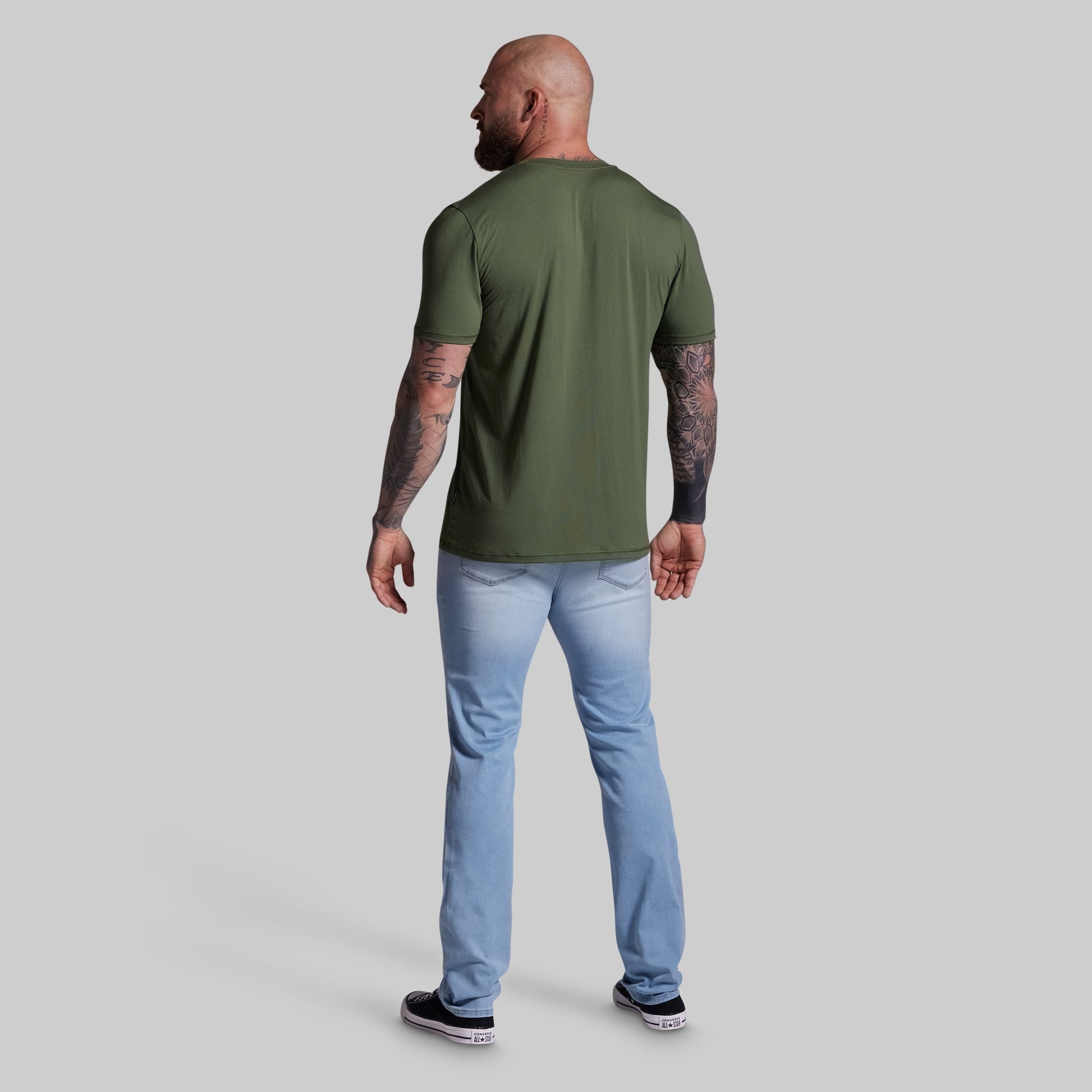 Man wearing a green t-shirt and light blue jeans on a gray background