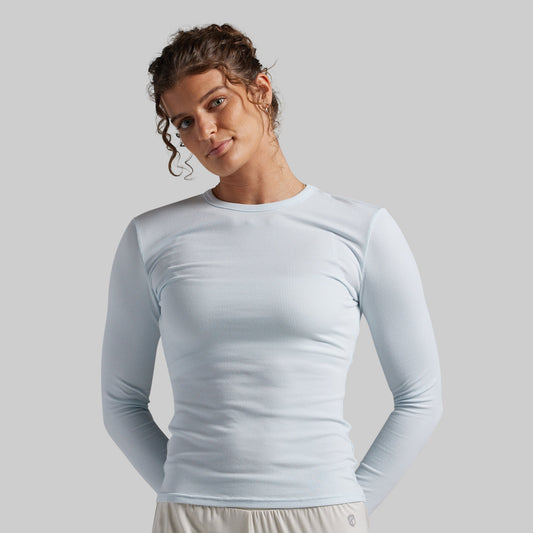 A woman wearing a light blue long-sleeve crewneck athletic top, photographed against a solid light gray background.