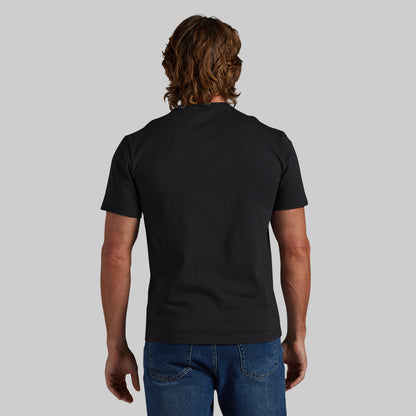 A man viewed from behind wearing a plain black short-sleeve t-shirt and blue jeans, standing against a solid light gray background.