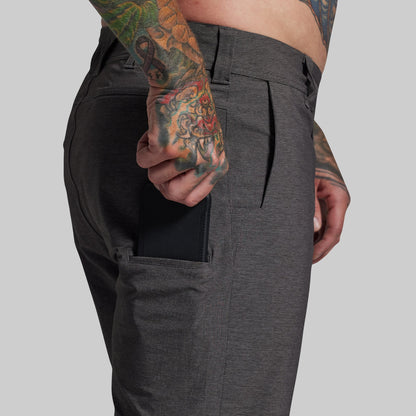 Person wearing dark gray shorts with a tattooed arm holding a phone.