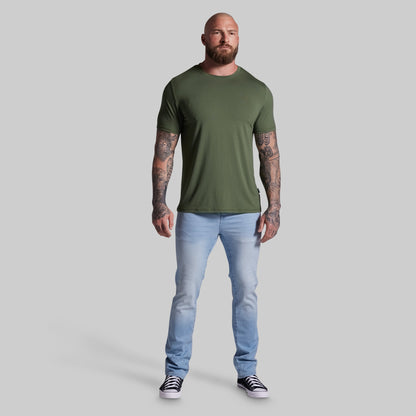 Man wearing an olive green t-shirt and light blue jeans on a gray background