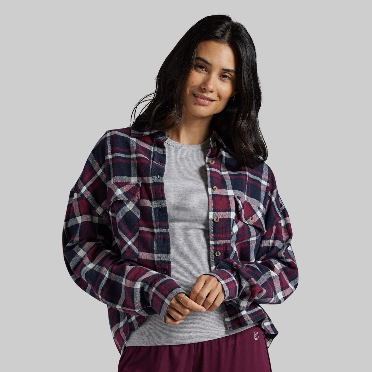 A woman modeling a long-sleeve button-up plaid shirt in burgundy, navy, and white over a heather gray t-shirt.