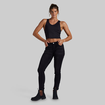 A woman modeling black skinny jeans with black Chelsea boots, standing against a solid light gray background.