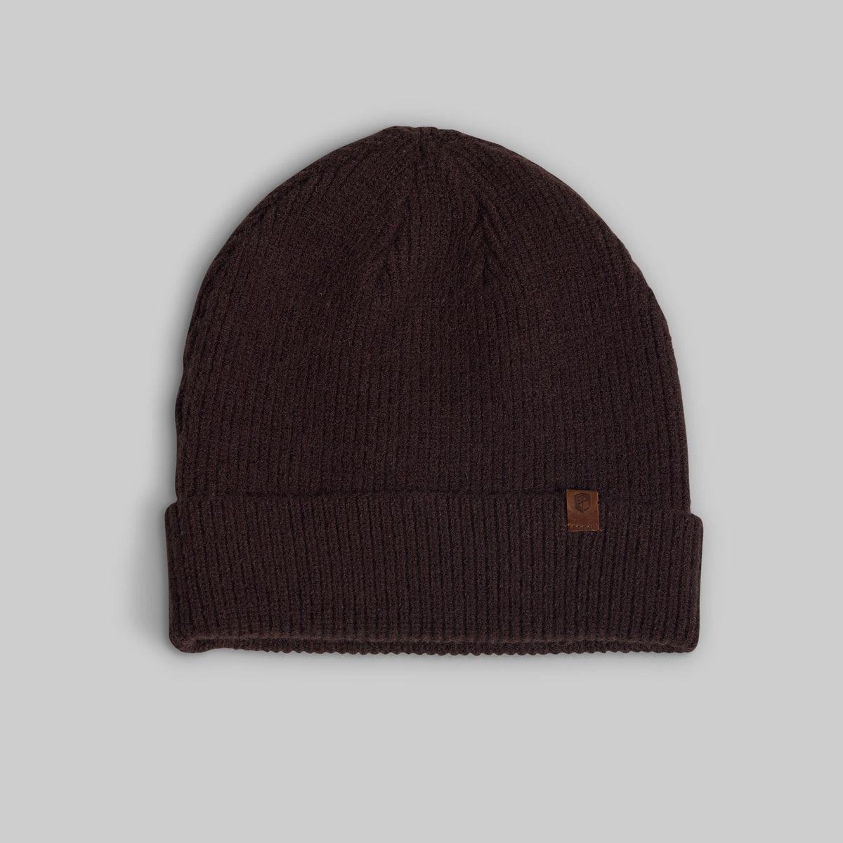 A dark brown ribbed knit beanie hat with a small brown leather logo patch on the side, displayed against a neutral gray background.