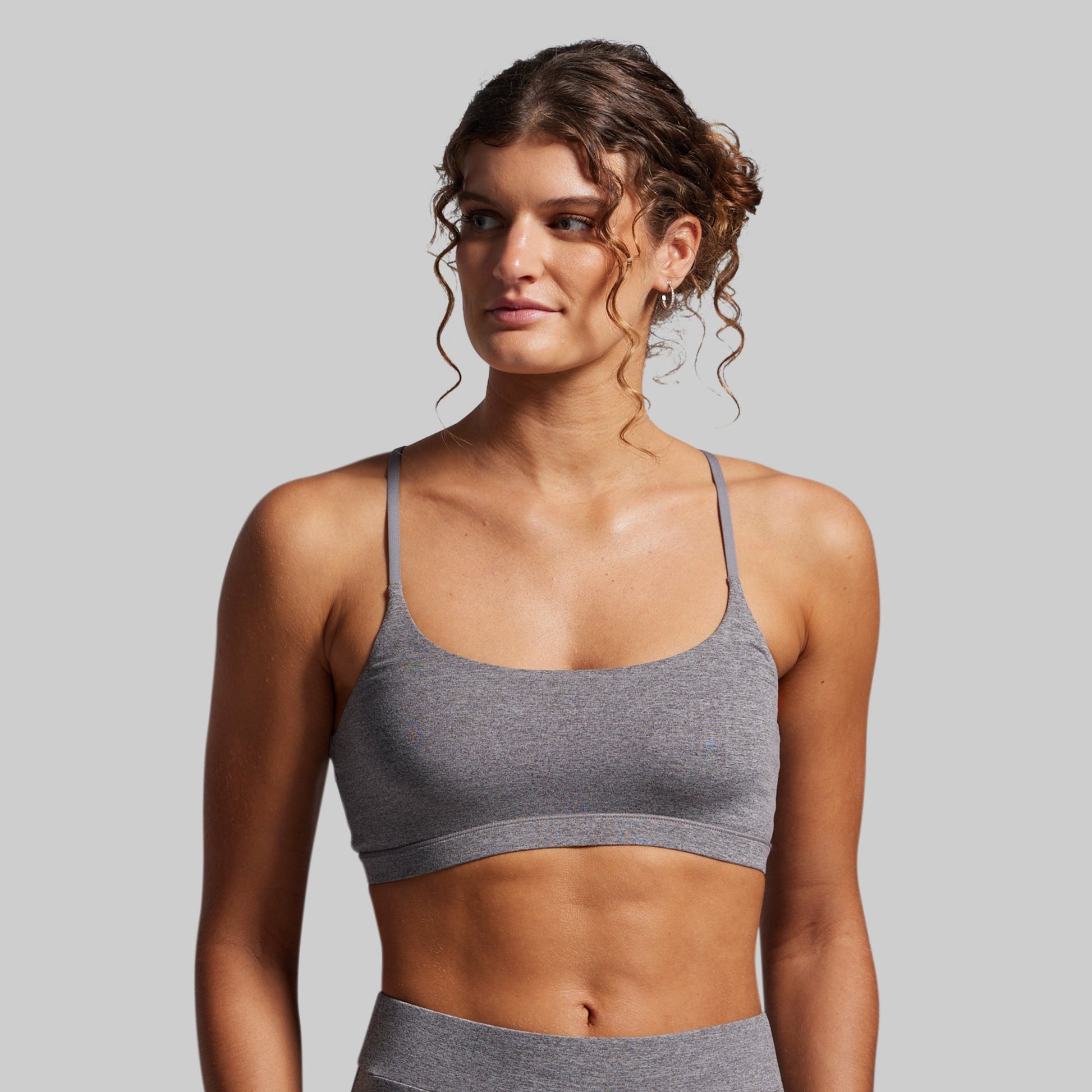 Woman wearing a gray sports bra and leggings against a plain background