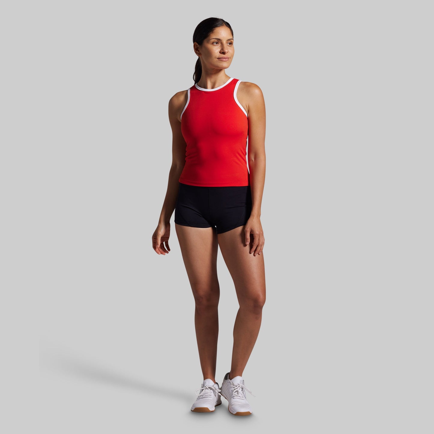 Woman wearing a red tank top and black shorts on a gray background