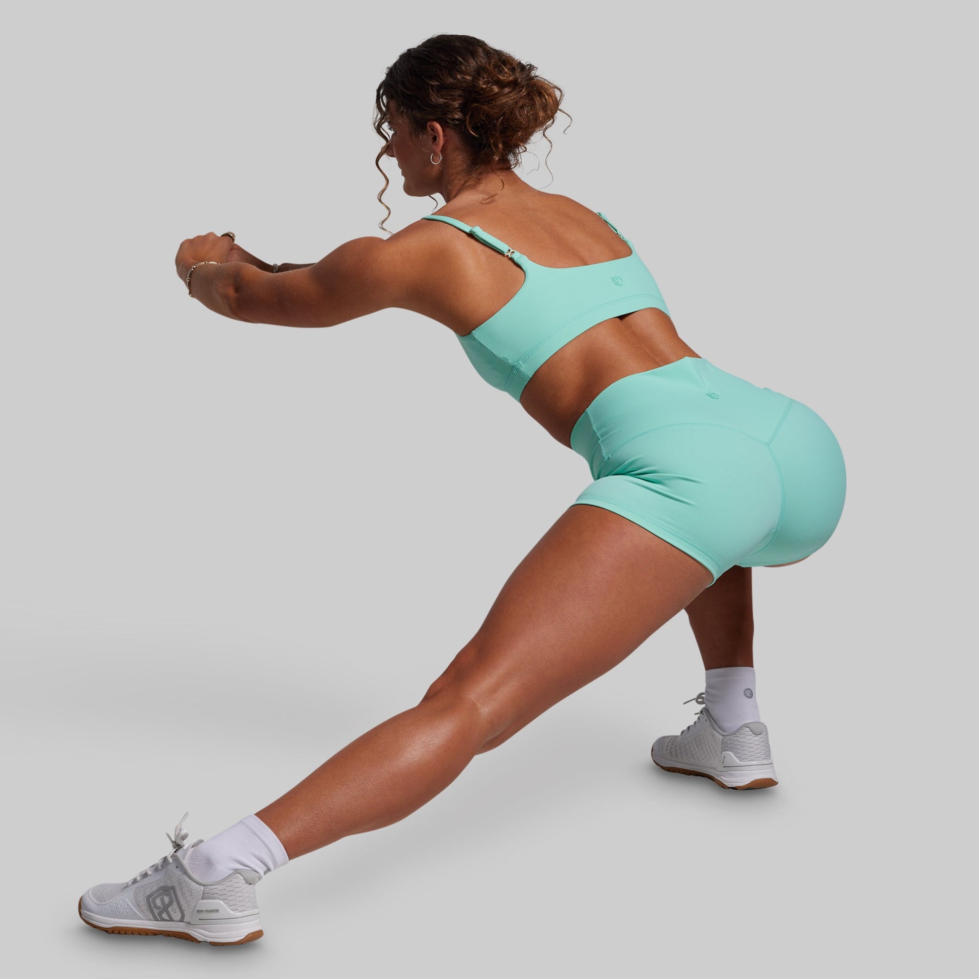 Person in teal athletic wear performing a lunge on a plain background
