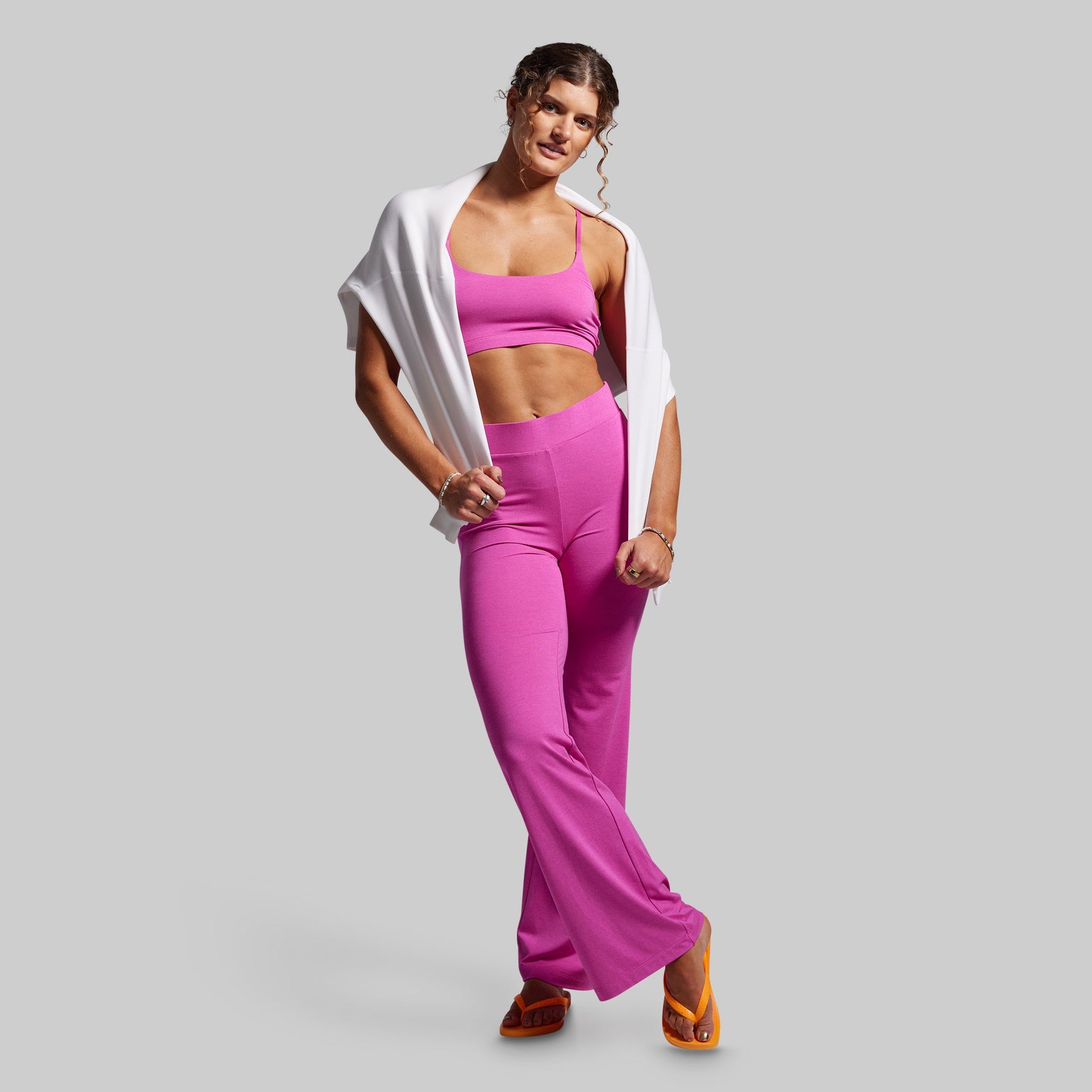 Woman wearing a pink sports bra and leggings with a white jacket on a gray background